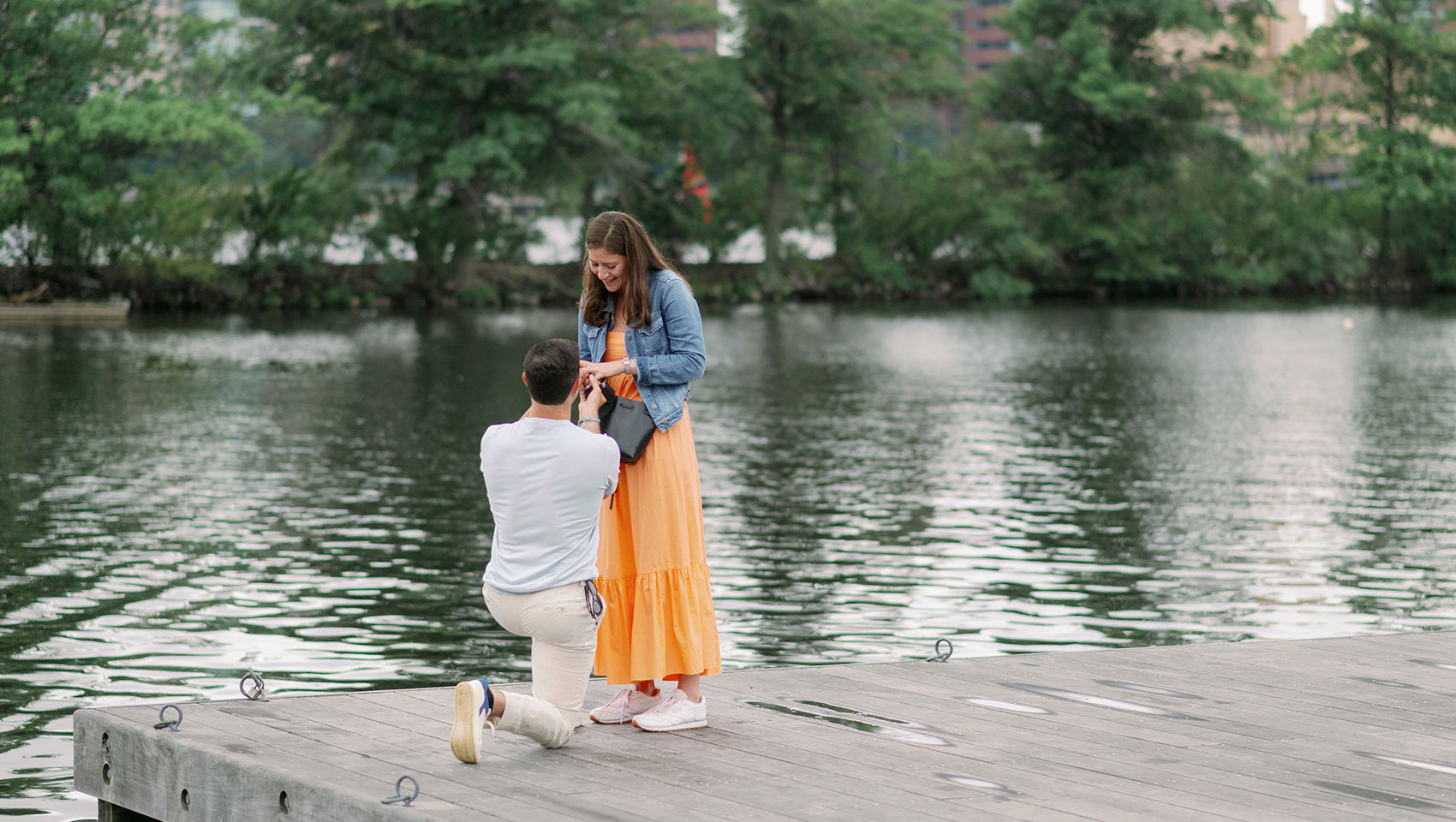 a person kneeling on a dock proposing to another person